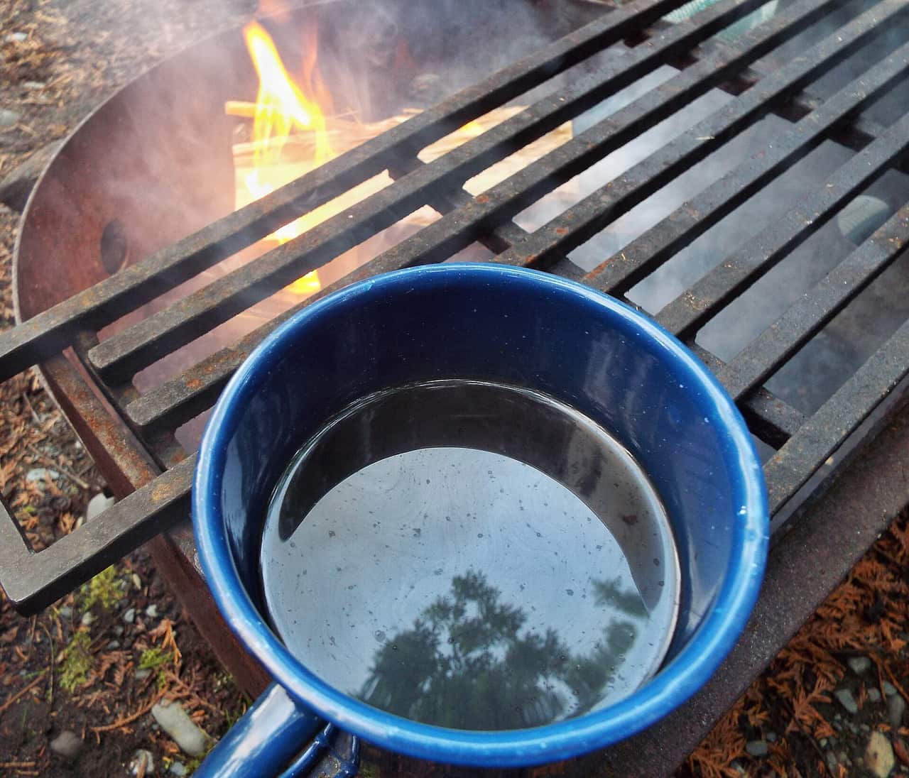 A coffee pot and enamel mug beside a camp stove at a campsite