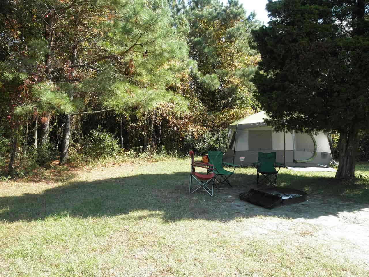 A campsite with a tent, folding chairs and a fire ring under trees
