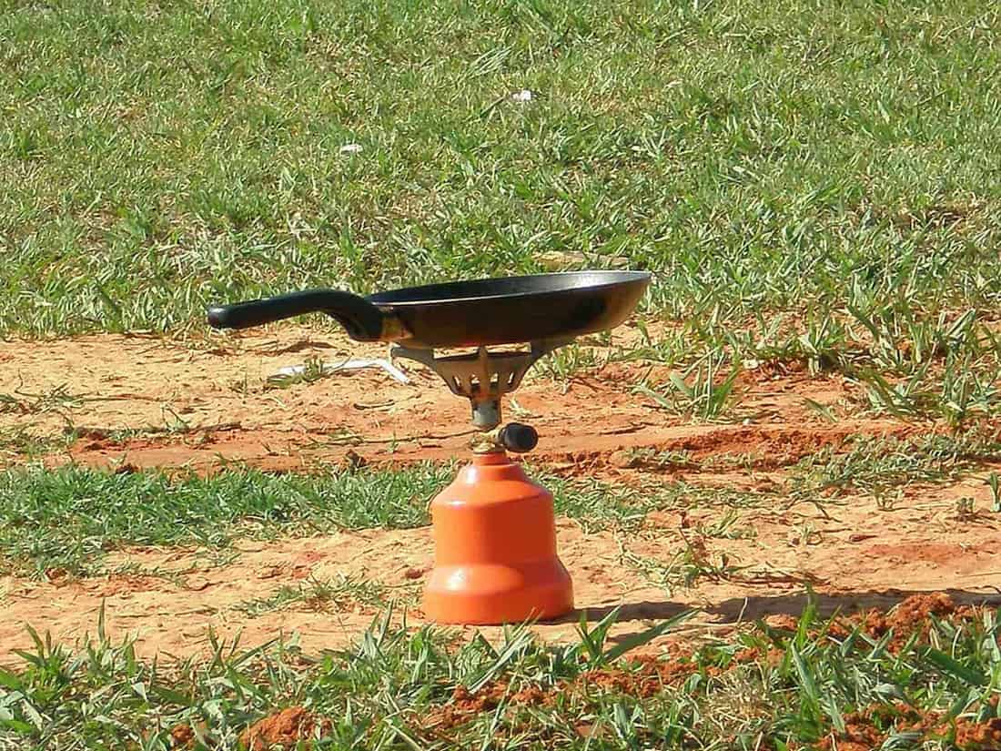 A two-burner camp stove set up on a picnic table with a pan on the heat