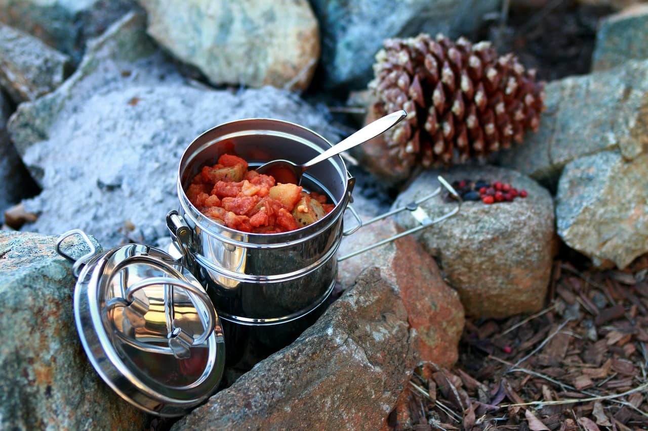 A one-pot meal cooking on a camp stove at a picnic table