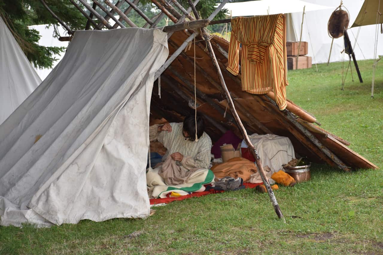 A furnished canvas tent with a bed, beside a simple dome tent