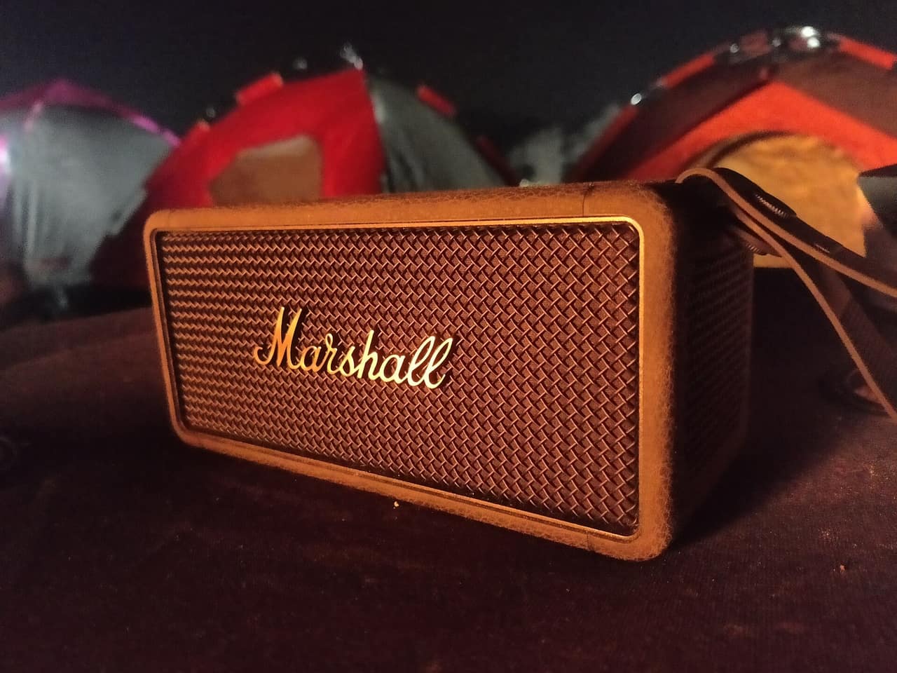 A portable Bluetooth speaker sitting in front of tents at night