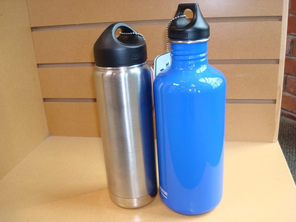 A clear plastic bottle beside an insulated steel bottle on a rock